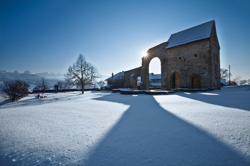 Die Ruine des ehemaligen Cluniazenserklosters Rueeggisberg erstrahlt im Gegenlicht der abendlichen Wintersonne. Im Hintergrund die majestaetische Gantrischkette.