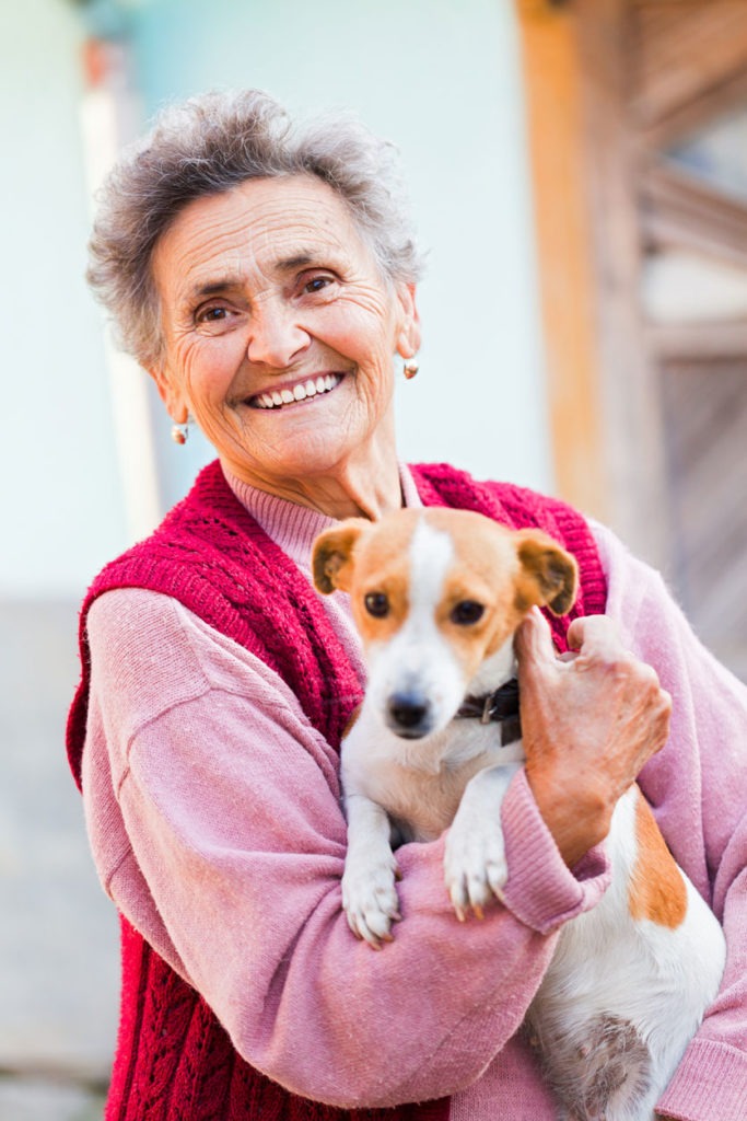 Eine glückliche Seniorin hält ihren Hund auf dem Arm.