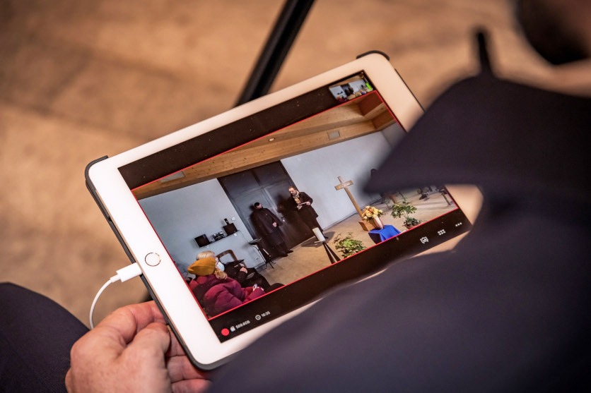 Online trauern: Zu sehen ist ein iPad, auf dem eine Trauerfeier übertragen wird. Zeitlupe.