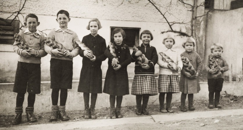 Schwarzweissfoto: 8 Kinder stehen in einer Reihe, jedes hat einen Zopf in der Hand.
