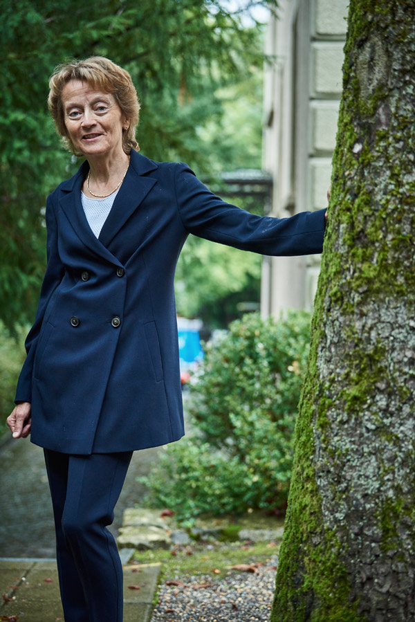 Eveline Widmer-Schlumpf, Praesidentin Pro Senectute, steht an einen Baum gelehnt im Innenhof der Pro Senectute Geschäftsstelle.