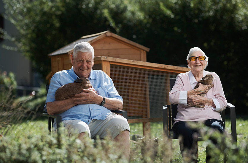 Zwei Bewohner des Altersheims Salem in Ennenda vor einem Hasenstall, finanziert von der Hatt-Bucher-Stiftung, mit Hasen auf dem Schoss.