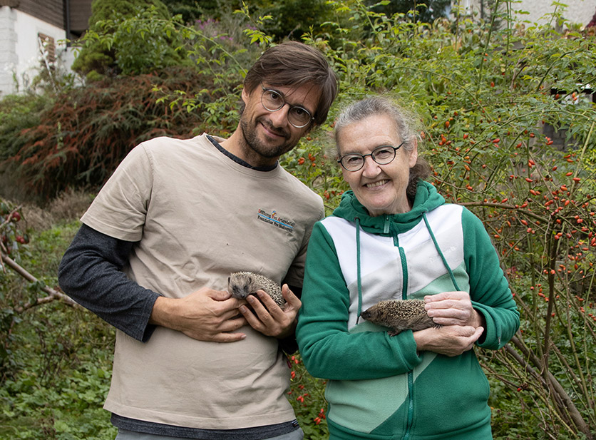 Eine ältere Frau und ein junger Mann halten jeweils einen Igel auf dem Arm und lächeln in die Kamera.