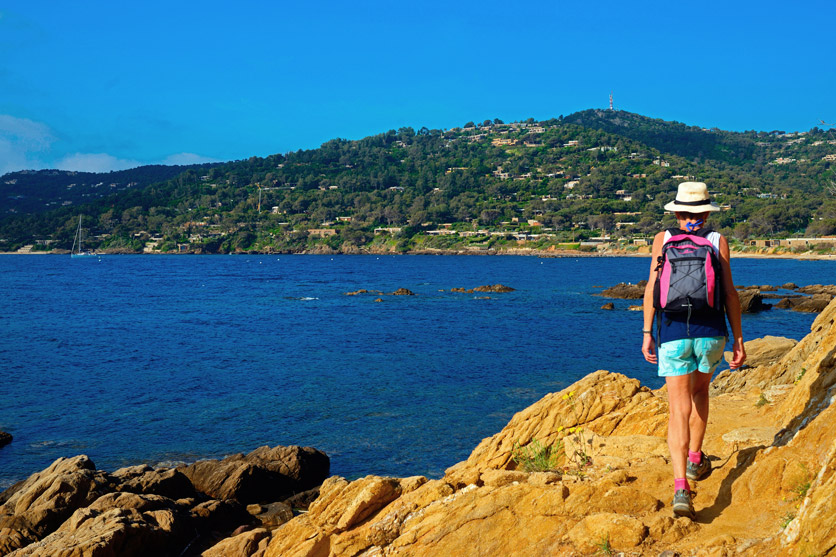 Eine Frau wandert an der Küste der Côte d'Azur über Felsen dem Wasser entlang.