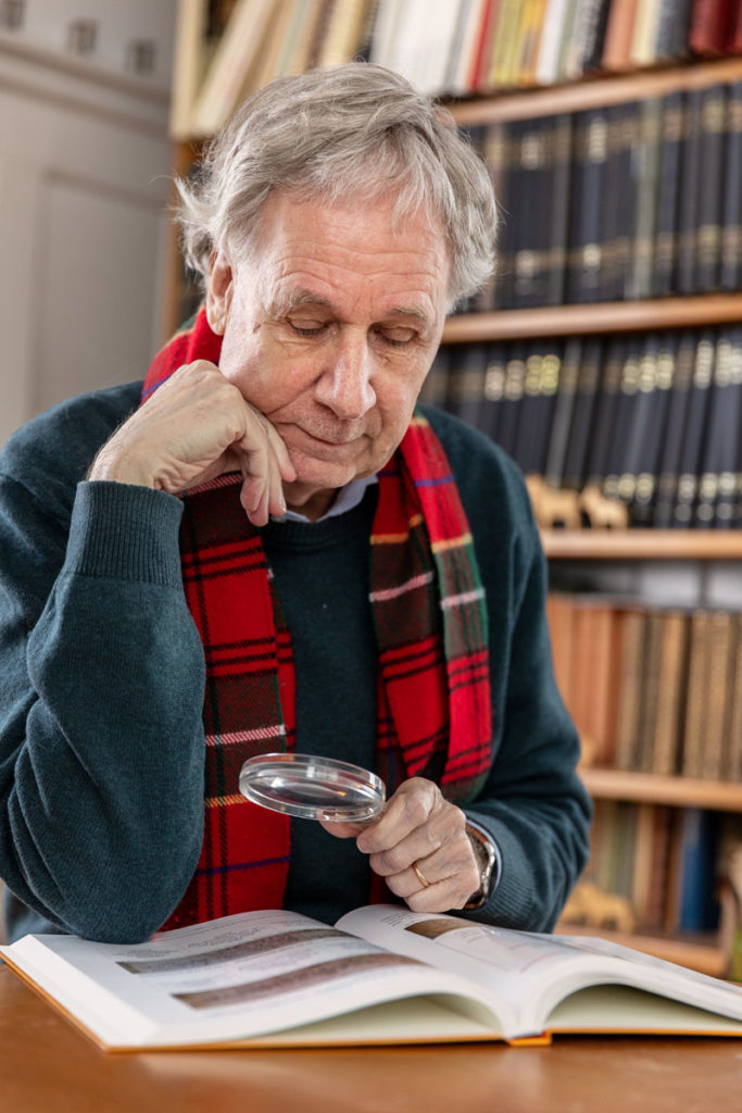 Prof. Dr. François Höpflinger schaut mit einer Lupe ein Buch an.