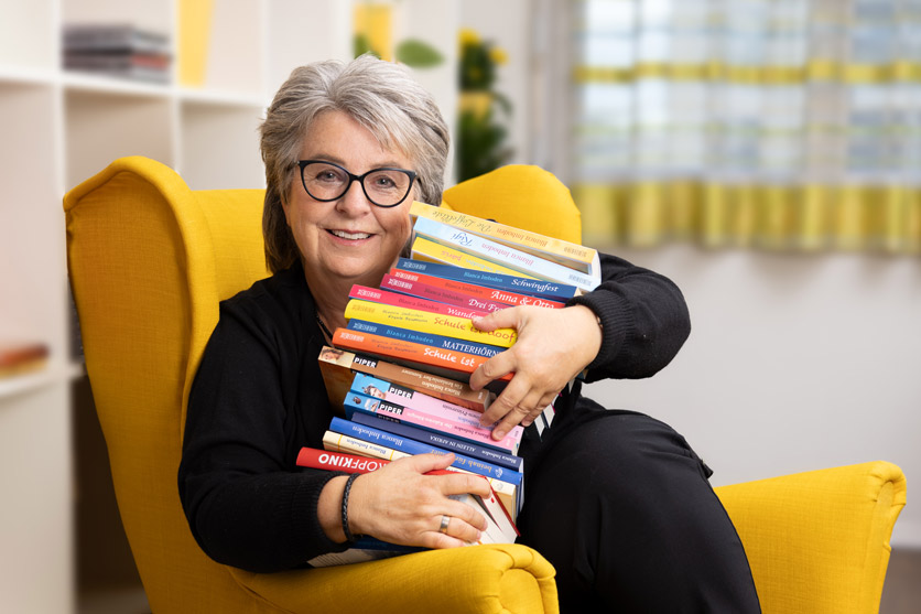 Portrait von Blanca Imboden mit Büchern auf ihrem Lesesessel. 