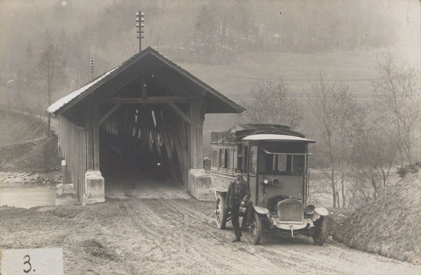 Das erste Postauto und sein Fahrer um 1906 vor einer gedeckten Holzbrücke.