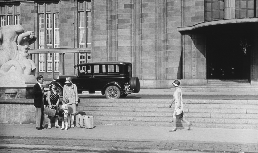 Anno 1930: Ein Junge mit blonden Locken steht mit Erwachsenen und Koffern vor dem Badischen Bahnhof