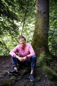 Portrait von Coach Martin Rohner im pinken Pullover im Wald unter einem Baum.