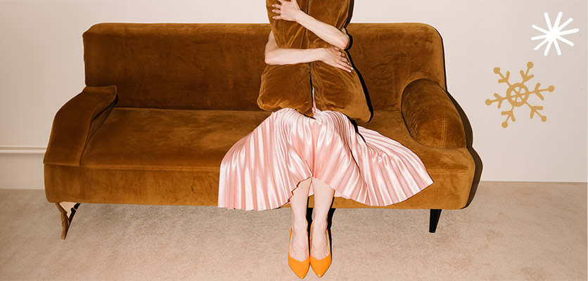 Eine Frau sitzt auf einem braunen Sofa und hält Kissen vor das Gesicht. 