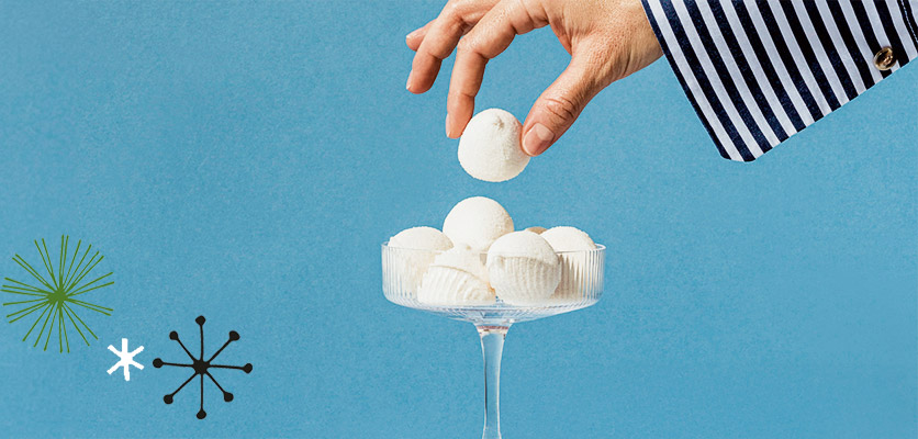 Schönes für daheim: eine Hand nimmt weisse Pralinen aus einer Glasschale, blauer Hintergrund