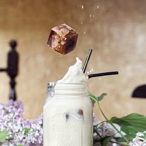 Ein Eiswürfel aus Kaffee fällt in ein Glas Milch