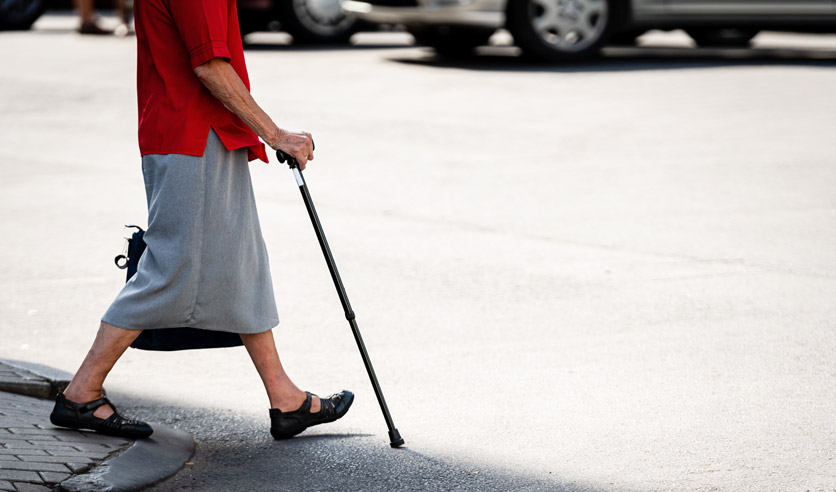 Eine Frau mit Gehstock überquert die Strasse.